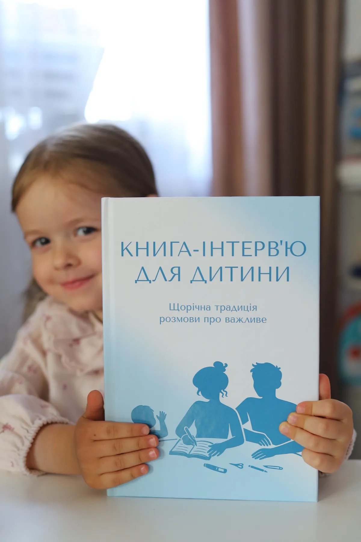 Девочка выглядывает из-за книги-интервью для ребёнка